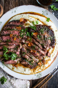 a large platter of whipped cauliflower with two sliced steaks over top