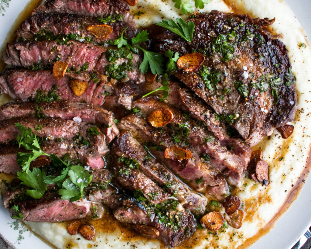 a large platter of whipped cauliflower with two sliced steaks over top