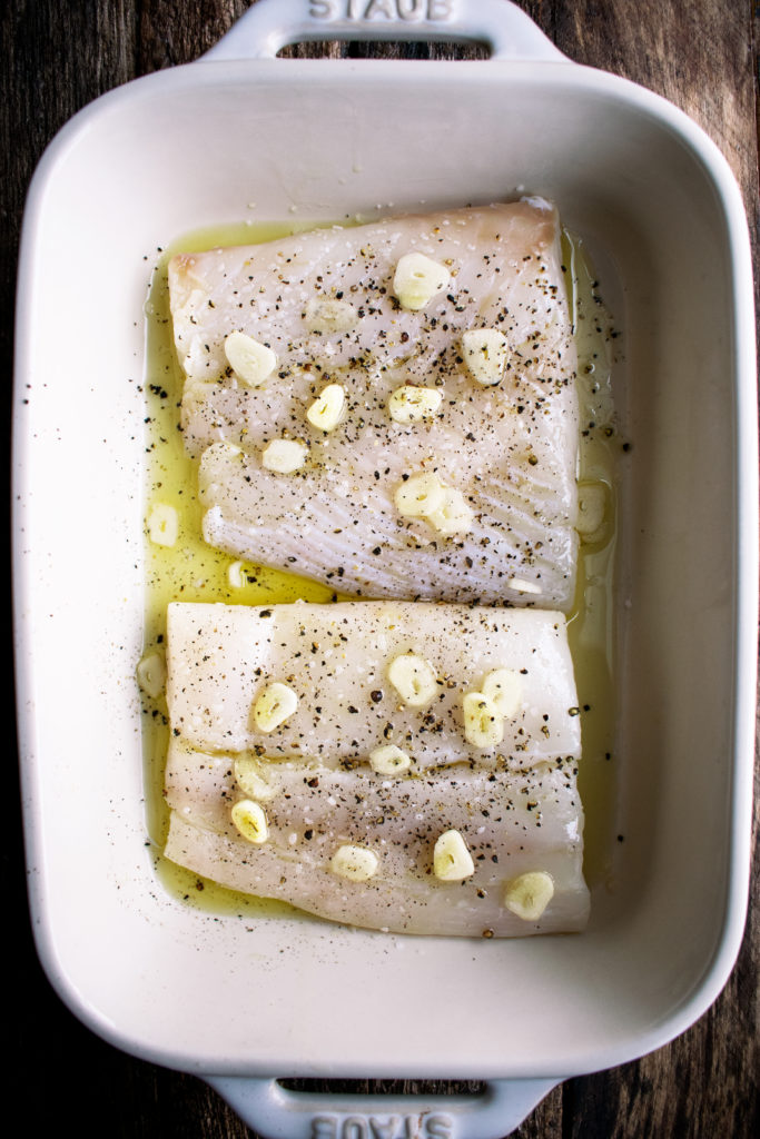 raw halibut seasoned with black pepper, garlic, and olive oil in a baking dish