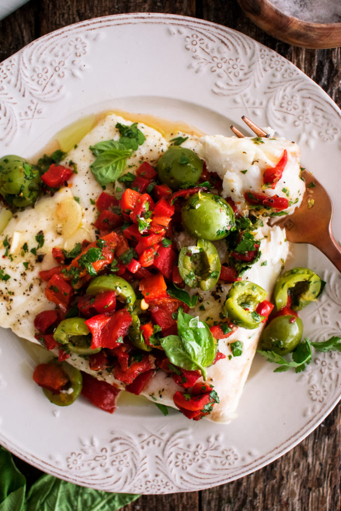 a piece of roasted halibut topped with red pepper and olive relish on a plate
