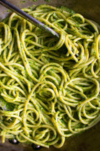 pasta being tossed in the pesto sauce