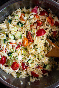 orzo salad being mixed in a bowl