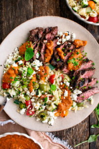 finished plate of skirt steak drizzled with the red peppers sauce and served with the orzo salad alongside