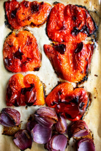 red peppers and red onions roasting on a sheet pan