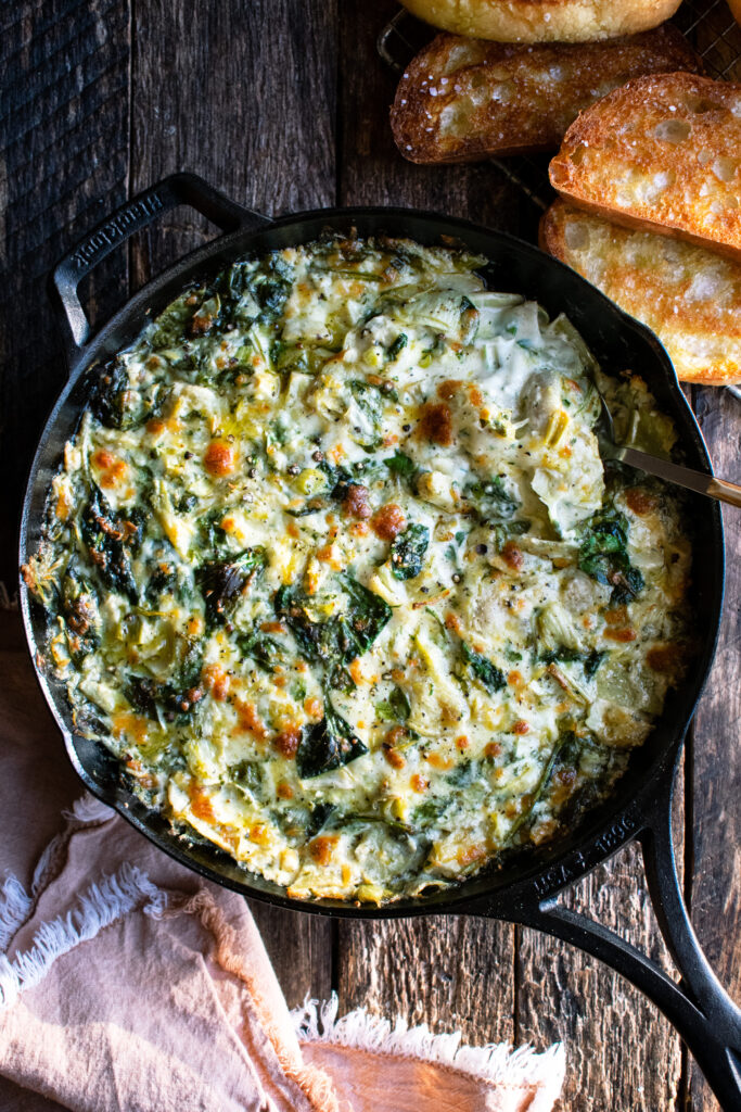 Cheesy Baked Spinach Artichoke Dip in a skillet with toasted bread on the side