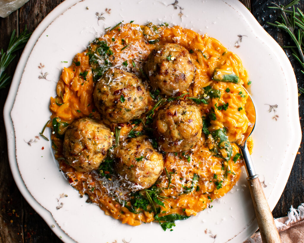 plate of Baked Rosemary Chicken Meatballs over tomato orzo