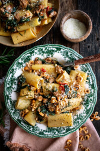 two bowls of spicy paccheri with sausage and greens topped with pecorino cheese and hazelnuts