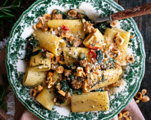 one bowl of spicy paccheri with sausage and greens topped with pecorino cheese and hazelnuts