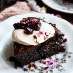 a slice of Flourless Chocolate Cherry Cake on a plate with whipped cream and cherry jam on top