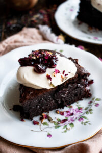 a slice of Flourless Chocolate Cherry Cake on a plate with whipped cream and cherry jam on top