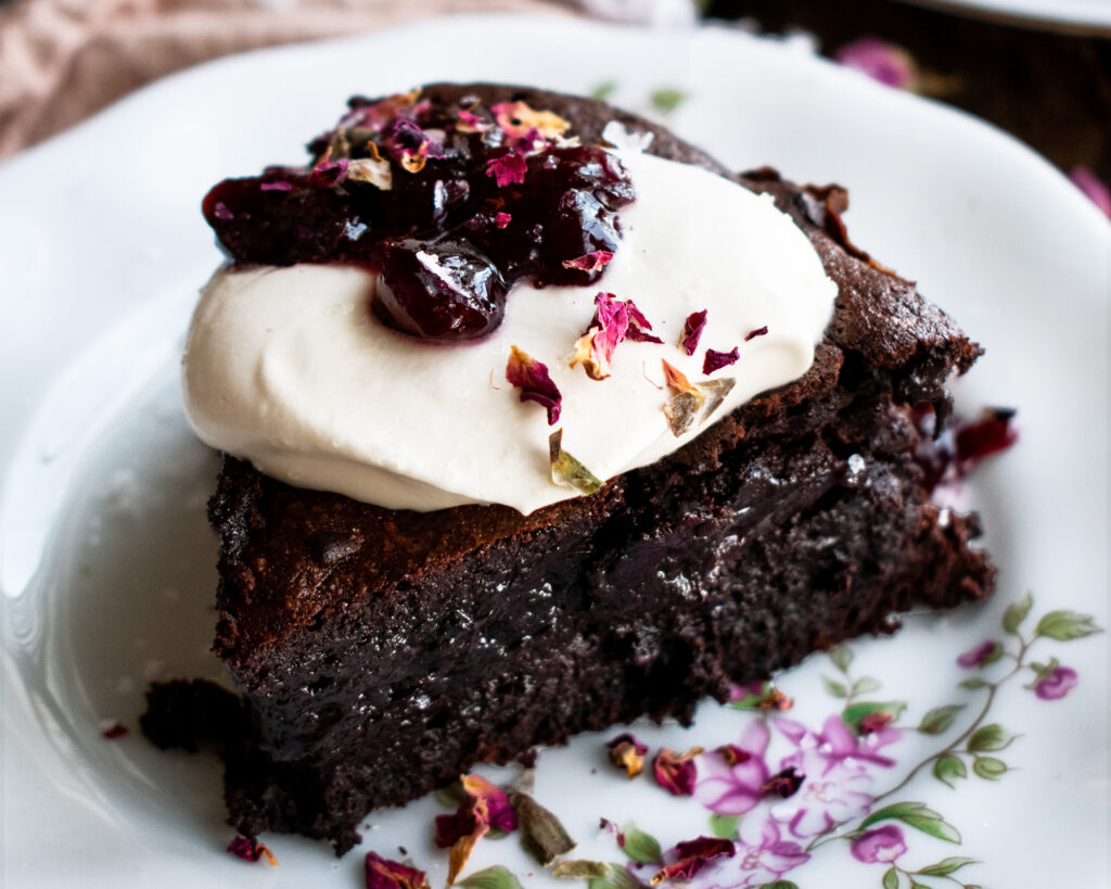 a slice of Flourless Chocolate Cherry Cake on a plate with whipped cream and cherry jam on top