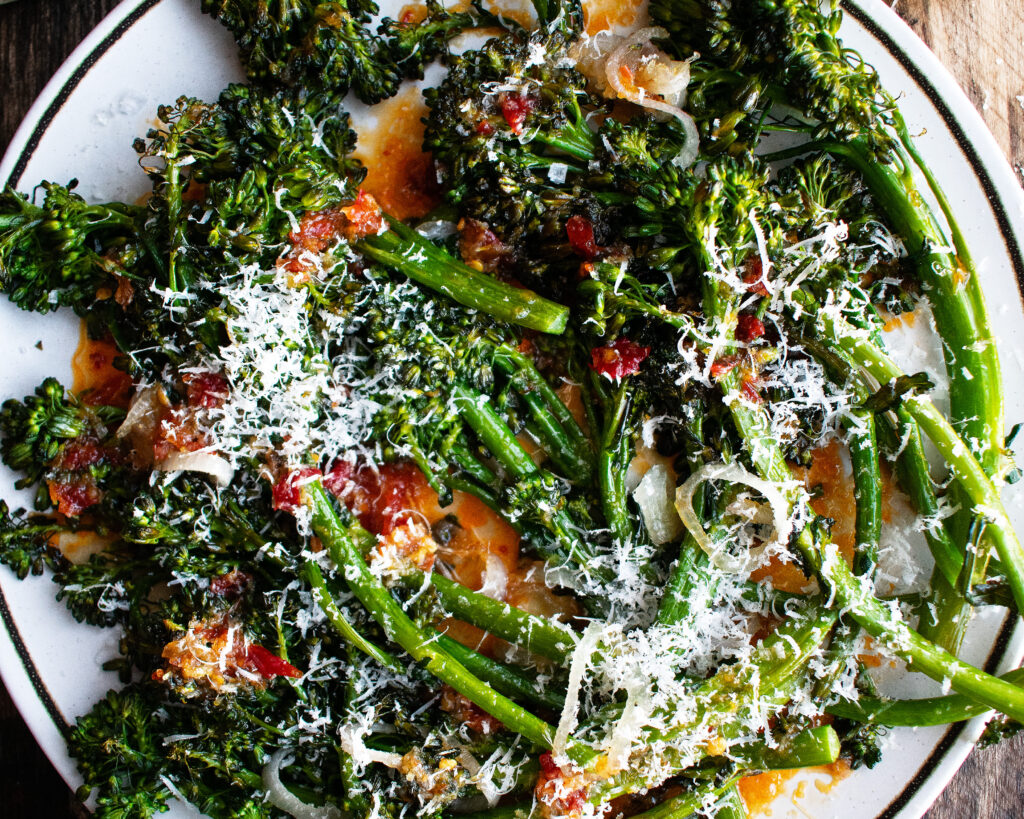 Roasted Broccolini on a plate with calabrian chile vinaigrette and parmesan over top