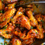 roasted chicken wings being tossed with the honey buffalo sauce in a mixing bowl