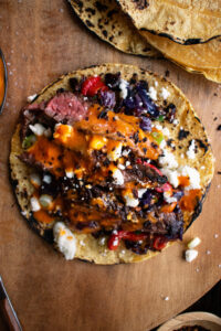 one steak taco with chipotle sauce & roasted cabbage slaw on a board