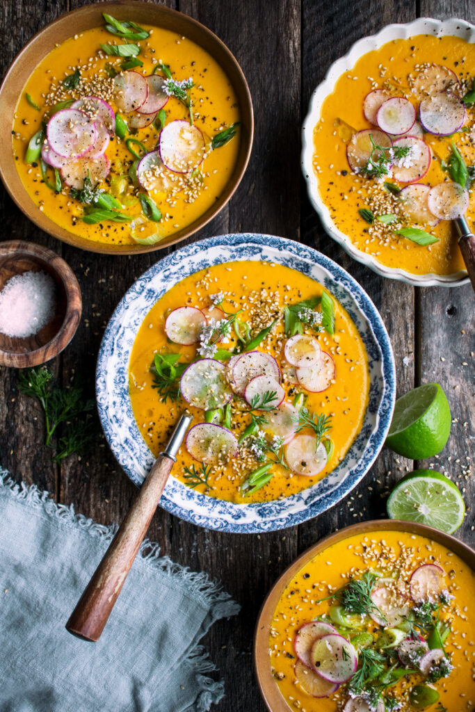 four bowls of Creamy Tahini Carrot Soup with radishes and green onions
