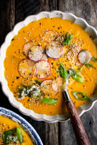 one bowl of Creamy Tahini Carrot Soup with radishes and green onions