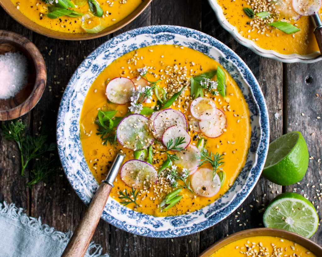 one bowl of Creamy Tahini Carrot Soup with radishes and green onions