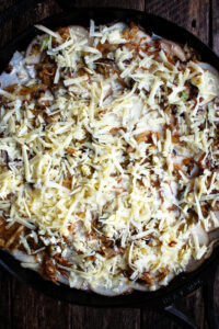 a skillet of potato slices layered with cabbage and topped with cheddar before going into the oven