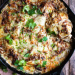 a skillet of scalloped potatoes out of the oven with melted cheddar and herbs over top