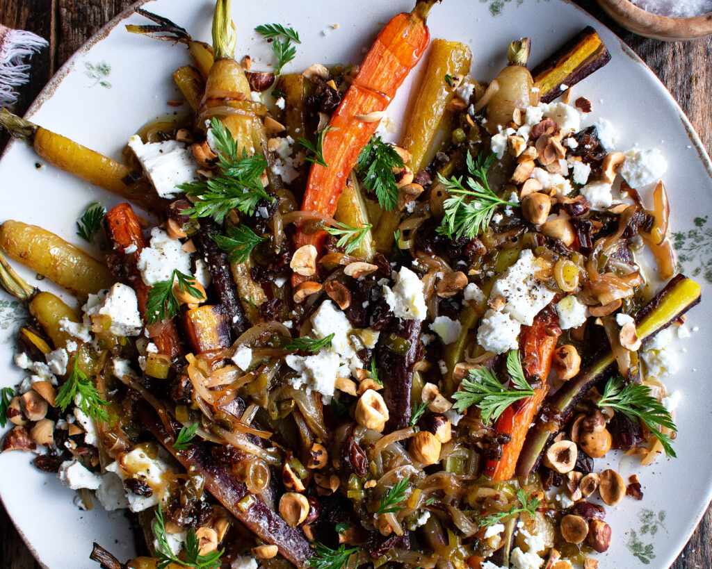 roasted carrots on a plate topped with scallion vinaigrette, feta, and hazelnuts