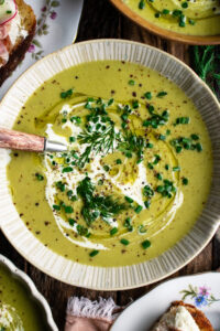 a bowl of Asparagus Soup topped with a drizzle of cream and fresh herbs