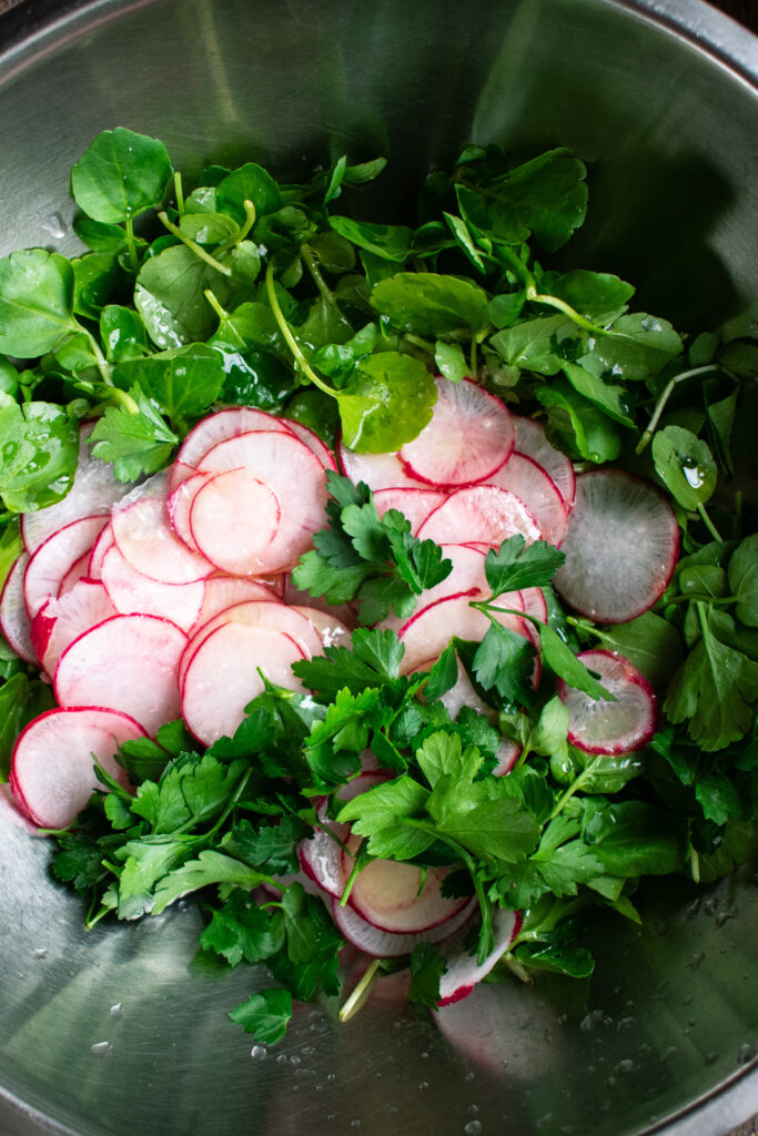 watercress salad with radishes and parsley in a mixing bowl