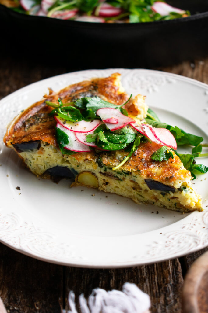one slice of the Potato & Gruyère Frittata on a plate with the watercress salad over top