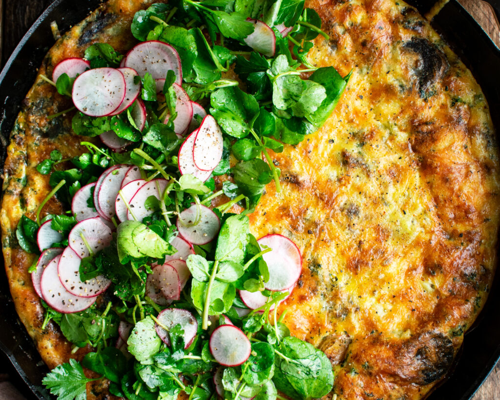 finished Potato & Gruyère Frittata in a skillet with watercress salad over top