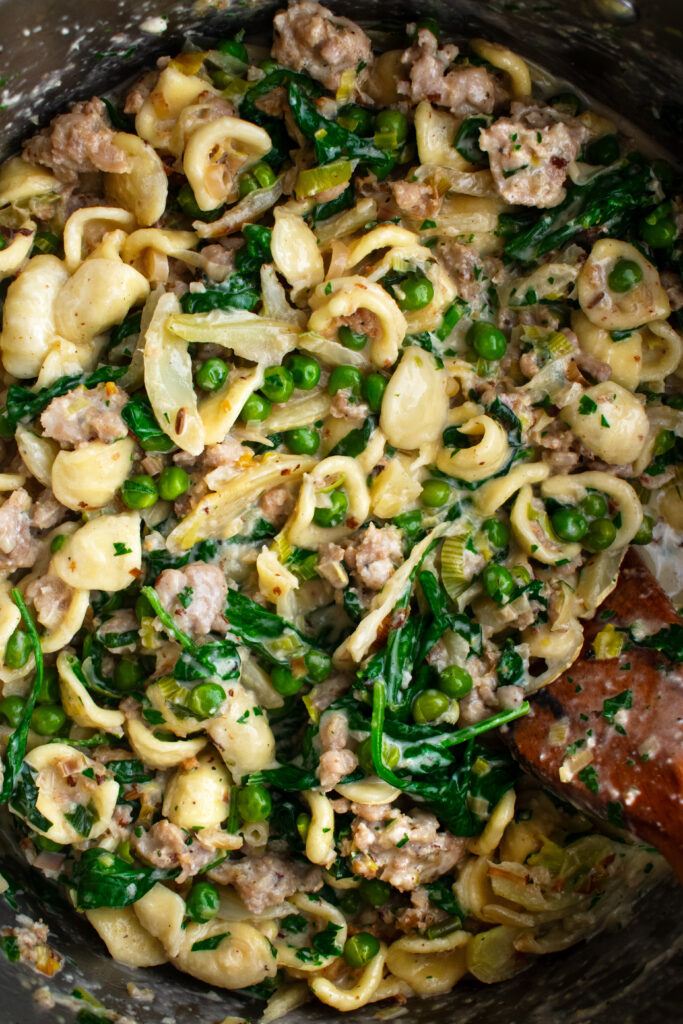 Creamy Orecchiette with chicken sausage and spring vegetables in a pot being mixed