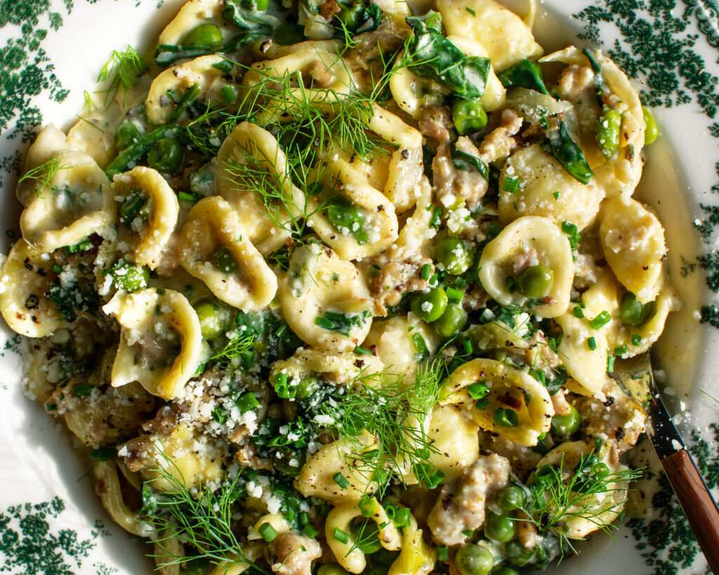 finished dish of Creamy Orecchiette with chicken sausage & spring vegetables in a bowl with herbs and cheese on top