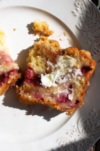 half of a slice of strawberry jam coffee cake with a smear of butter on a plate