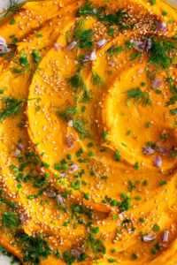 Paprika Roasted Carrot Hummus on a plate with herbs and sesame seeds on top