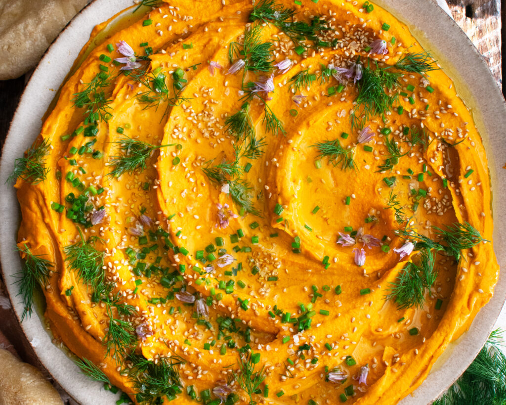 Paprika Roasted Carrot Hummus on a plate with herbs and sesame seeds on top