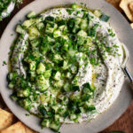 whipped feta dip on a plate with cucumber salad over top and pita chips on the side