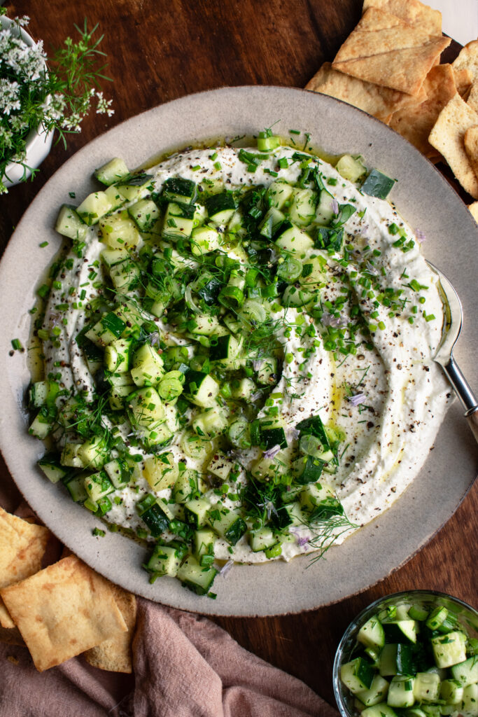 whipped feta dip on a plate with cucumber salad over top and pita chips on the side