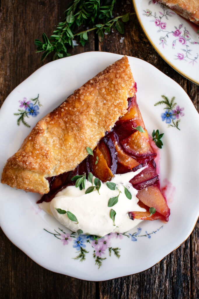 a slice of a Plum Galette topped with whipped mascarpone and fresh thyme