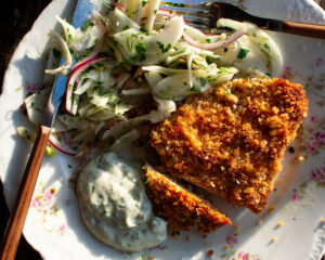 a plate of walnut crusted chicken and fennel slaw with herby mayo alongside