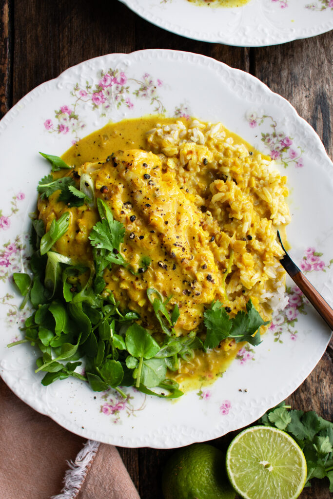 a plate of yellow curry poached cod over rice with watercress & herbs on top