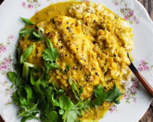 a plate of yellow curry poached cod over rice with watercress & herbs on top