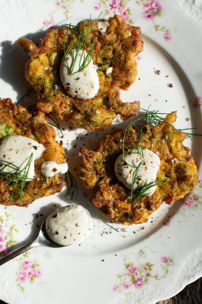 zucchini fritters on a plate with lemon yogurt sauce over top
