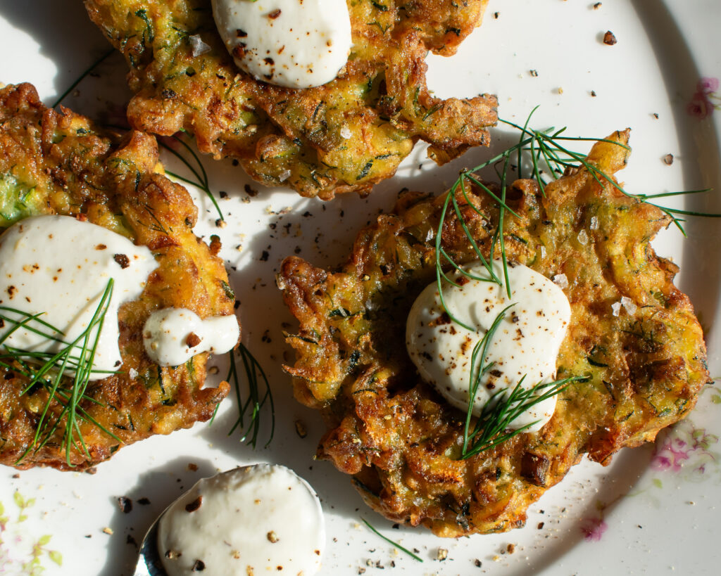 zucchini fritters on a plate with lemon yogurt sauce over top