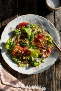 a plate of salad with butter lettuce, fennel, radish, blood oranges, basil, pistachios, and spicy citrus vinaigrette