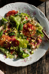 a plate of salad with butter lettuce, fennel, radish, blood oranges, basil, pistachios, and spicy citrus vinaigrette
