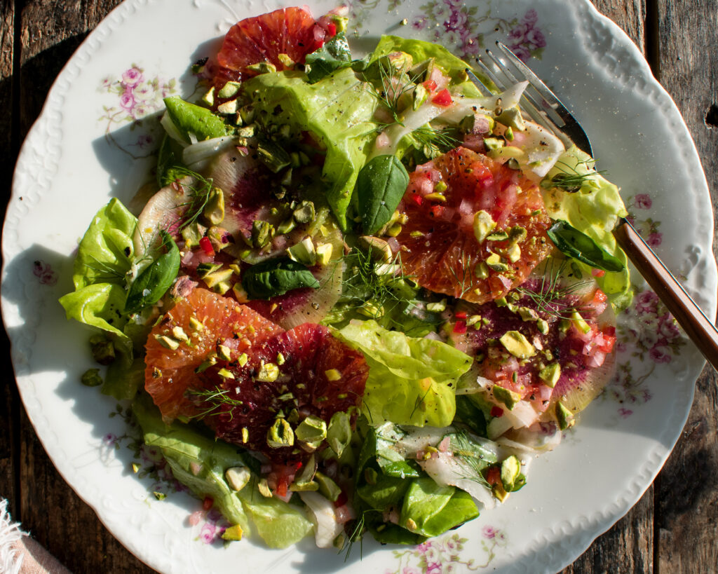 a plate of salad with butter lettuce, fennel, radish, blood oranges, basil, pistachios, and spicy citrus vinaigrette