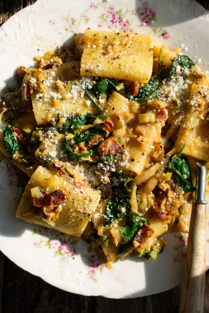 plate of paccheri with leeks, bacon, spinach, and pecorino over top