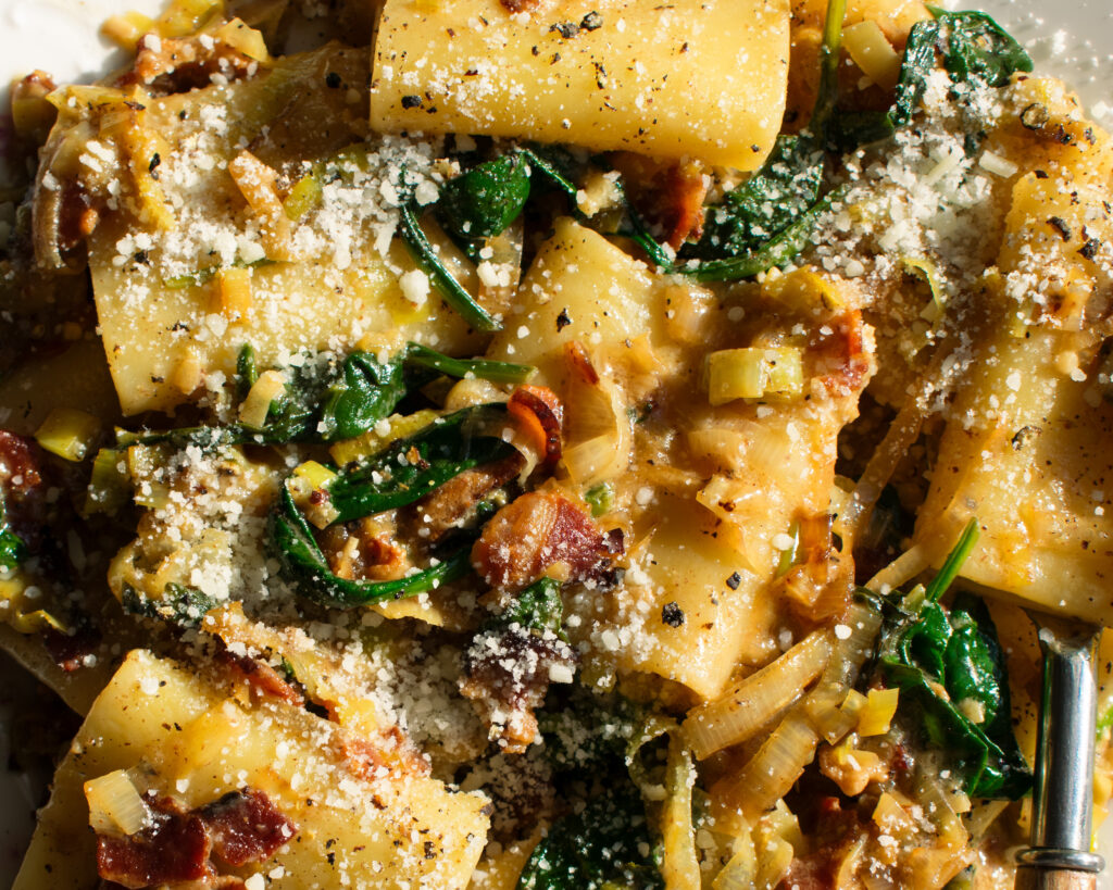 plate of paccheri with leeks, bacon, spinach, and pecorino over top