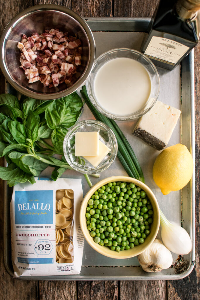 Ingredients on a tray: pancetta, basil, orecchiette, butter, peas, garlic, spring onion, lemon, pecorino, cream, and olive oil