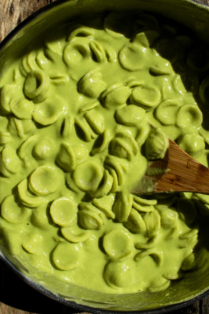 orecchiette being stirred with the creamy basil & pea sauce in a saute pan