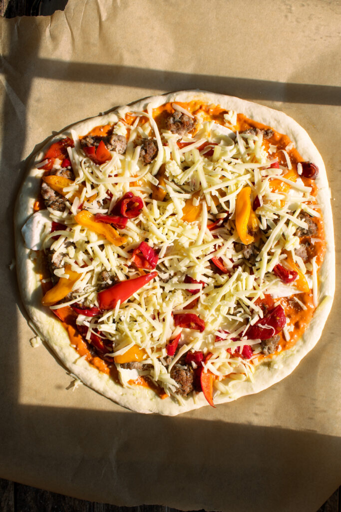 homemade pizza dough rolled out and topped with creamy vodka sauce, sausage, sweet peppers, fresh mozzarella, and fontina cheese