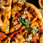 sausage & sweet pepper pizza sliced and topped with fresh basil